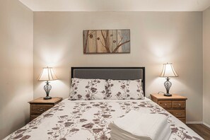 Ein Schlafzimmer mit einem Bett, zwei Nachttischen, zwei Lampen, einem kleinen Tisch und einem Wandbild.