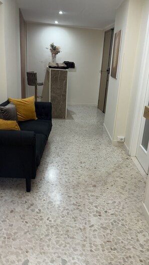 A hallway with a marble floor, a dark-colored sofa with cushions, a small table with a vase, and a door at the end. - In the city center, 150 meters from the Museum of the Riace Bronzes (Reggio Calabria)