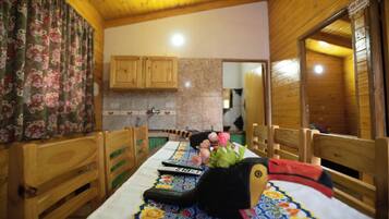 Interior de madera con una mesa para dos, una cortina floral y una zona de cocina con armarios de madera.