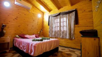 Dormitorio de cabaña de madera con cama, mesita de noche, lámpara y ventana con cortinas.