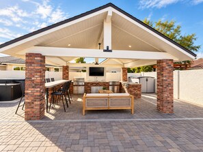 An outdoor patio with a grill, seating, and a TV mounted on the wall. - 4 Bedroom Retreat with Pool, hot tub, outdoor kitchen, arcades, sleeps 12 (Mesa)