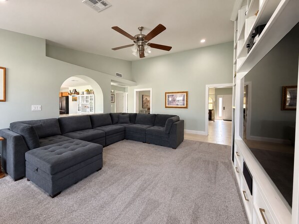 A living room with a sectional sofa, a ceiling fan, and a flat-screen TV. - 4 Bedroom Retreat with Pool, hot tub, outdoor kitchen, arcades, sleeps 12 (Mesa)
