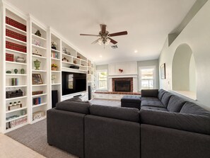 A living room with a sectional sofa, a flat-screen TV, a fireplace, and built-in shelving with various decorative items. - 4 Bedroom Retreat with Pool, hot tub, outdoor kitchen, arcades, sleeps 12 (Mesa)