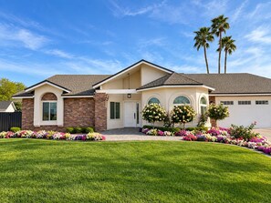 A two-story house with a brick facade, a garage, and a well-maintained lawn with colorful flower beds. - 4 Bedroom Retreat with Pool, hot tub, outdoor kitchen, arcades, sleeps 12 (Mesa)