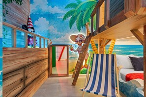 A room with a wooden deck, a beach-themed mural, a striped beach chair, and a bed with a view of the mural. - Sophisticated New Home Near Disney (2592SN) (Kissimmee)