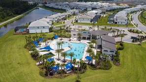 An aerial view of a residential area with a large swimming pool surrounded by houses, palm trees, and a river. - Sophisticated New Home Near Disney (2592SN) (Kissimmee)