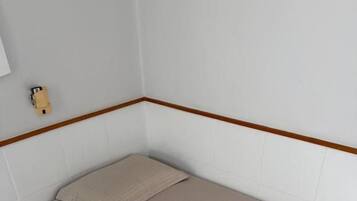 A single bed with a beige bedspread in a room with white walls and a wooden trim.
