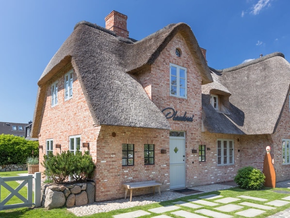 Ein Haus aus Ziegelsteinen mit einem Reetdach und einem kleinen Garten.