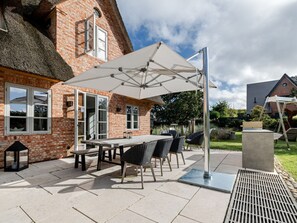 Eine Außenpatio mit Tisch und Stühlen, einem großen Sonnenschirm und einem Gebäude mit Backsteinfassade und strohgedecktem Dach.