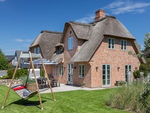 Ein Haus mit Strohdach und Backsteinwänden, einer Schaukel und einem gepflegten Rasen.
