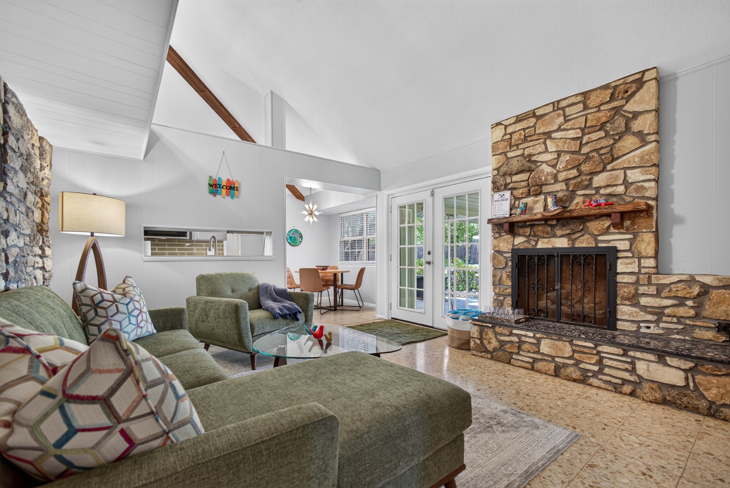 A modern living room with a stone fireplace, a green sofa, and a kitchen in the background.