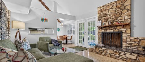 A modern living room with a stone fireplace, a green sofa, and a kitchen in the background.