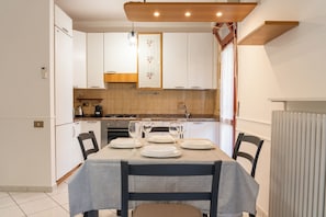 A modern kitchen with white cabinets, a dining table set for four, and a window with a view. - Emilia Suite Holiday (Modena)