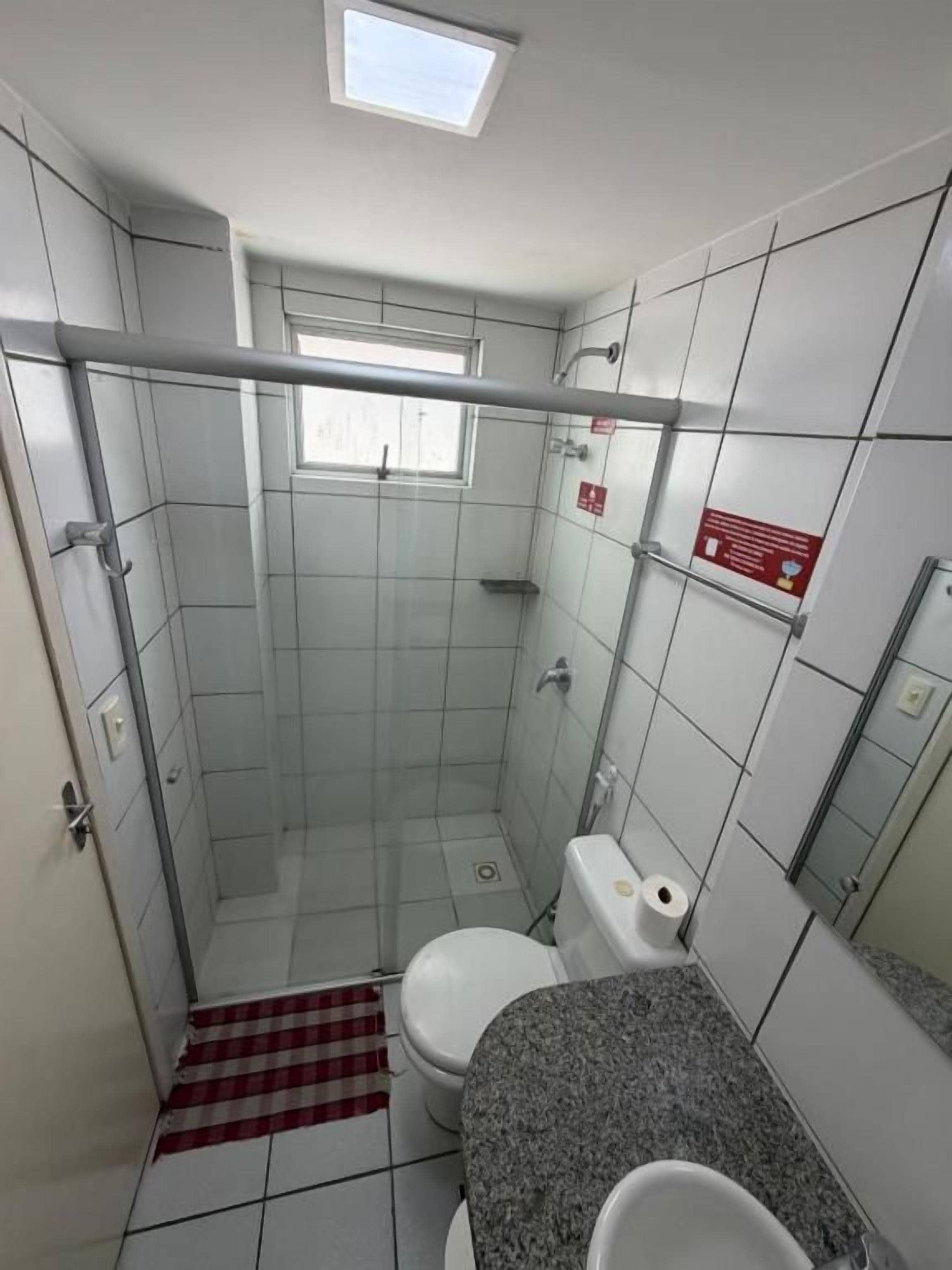 A small bathroom with a shower, toilet, and a window.