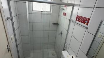 A small bathroom with a shower, toilet, and a window.
