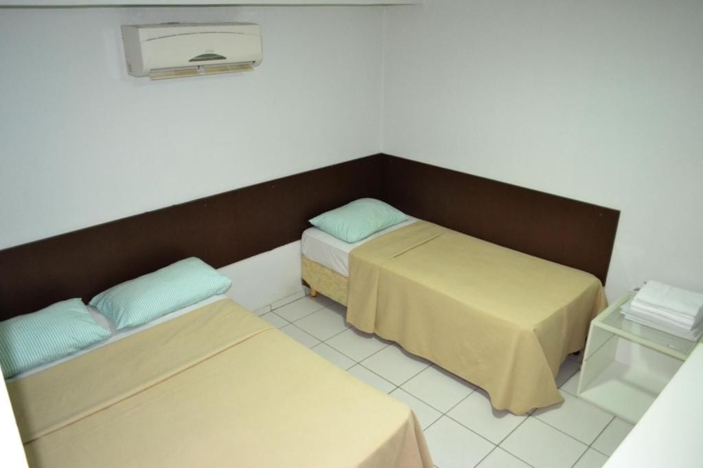 Una habitación pequeña y limpia con dos camas individuales, una mesita de noche y aire acondicionado instalado en la pared.