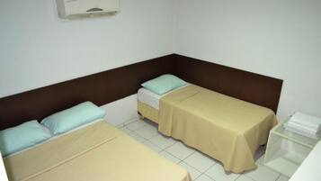 A small, clean room with two single beds, a bedside table, and a wall-mounted air conditioning unit.