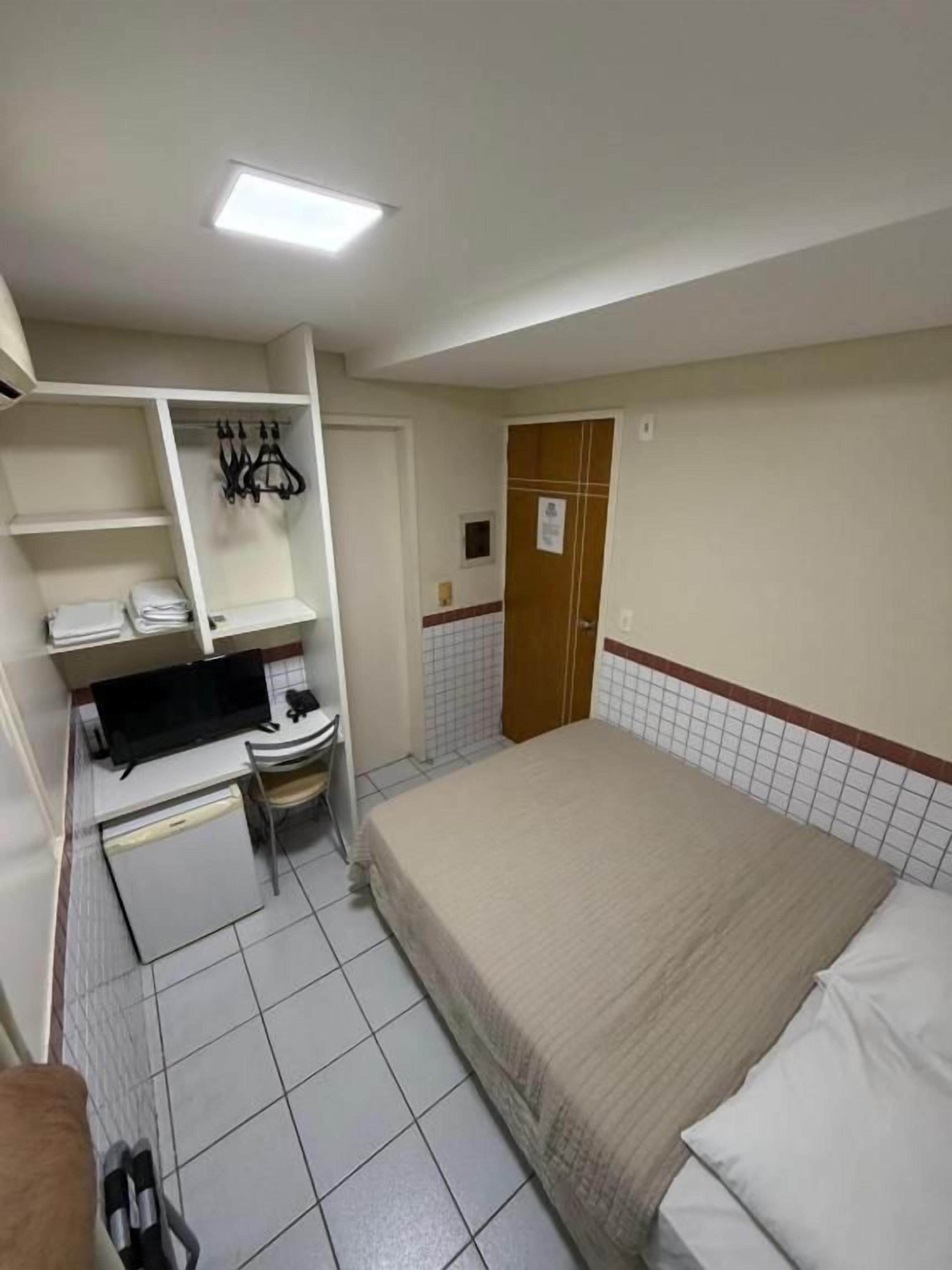 Una habitación de hotel pequeña y funcional, con cama, escritorio, silla y armario.