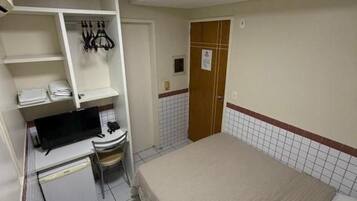 Una habitación de hotel pequeña y funcional, con cama, escritorio, silla y armario.