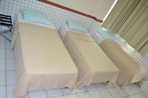 A room with three beds, each covered with a beige sheet, and a metal rack with a towel. - Rede Andrade Ideal (Teresina)