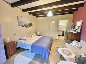 Un dormitorio con cama, mesita de noche y tocador. Hay una puerta que conduce a un baño y una kitchenette.