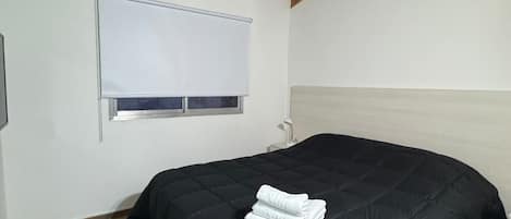 Een slaapkamer met een houten plafond, een bed met een zwart sprei en een raam met zonwering.