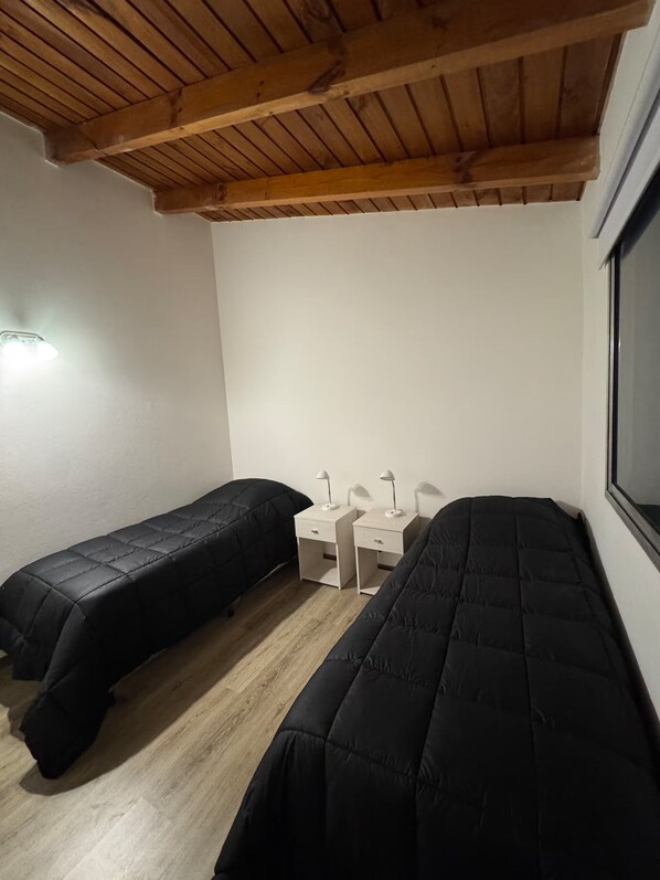 A room with two single beds, a small table with two lamps, and a window. - Depto cálido cerca del centro (San Carlos de Bariloche)