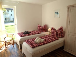 A room with two beds, a chair, a lamp, and a view of the outside. - Apartment 1.1 - Holiday Apartment in Graal-muritz (Graal Mueritz)