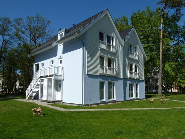 A two-story building with a balcony on the second floor, a staircase leading to the entrance, and a well-maintained lawn. - Apartment 1.1 - Holiday Apartment in Graal-muritz (Graal Mueritz)