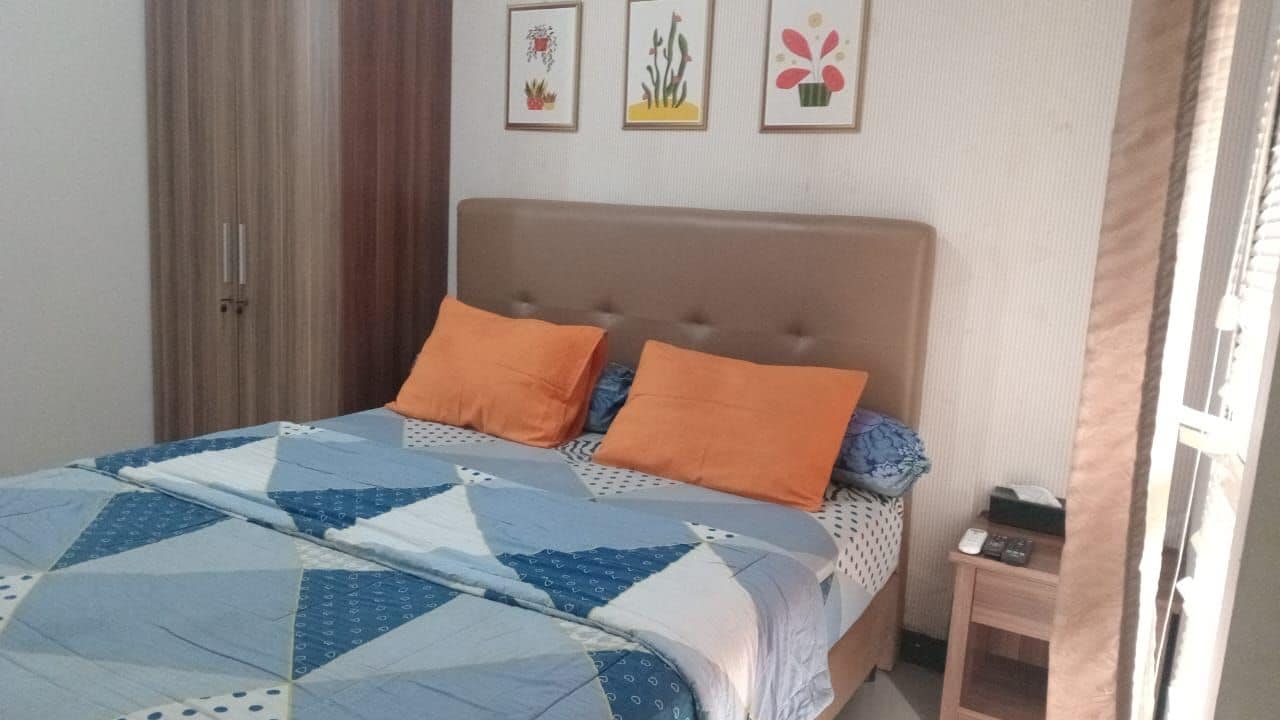 Un lit avec une couette, deux oreillers, une table de chevet avec une télécommande et une porte avec un rideau.