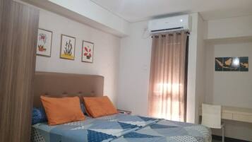 Un dormitorio con cama, dos almohadas, una mesita de noche, un equipo de aire acondicionado, una ventana con cortinas y decoración en la pared.