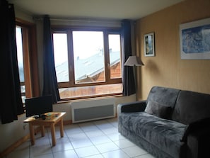 A living room with a sofa, a table with a board game, a window with curtains, a radiator, and a lamp. - Chambron Cb14 Center & View 4 Pers (Chatel)