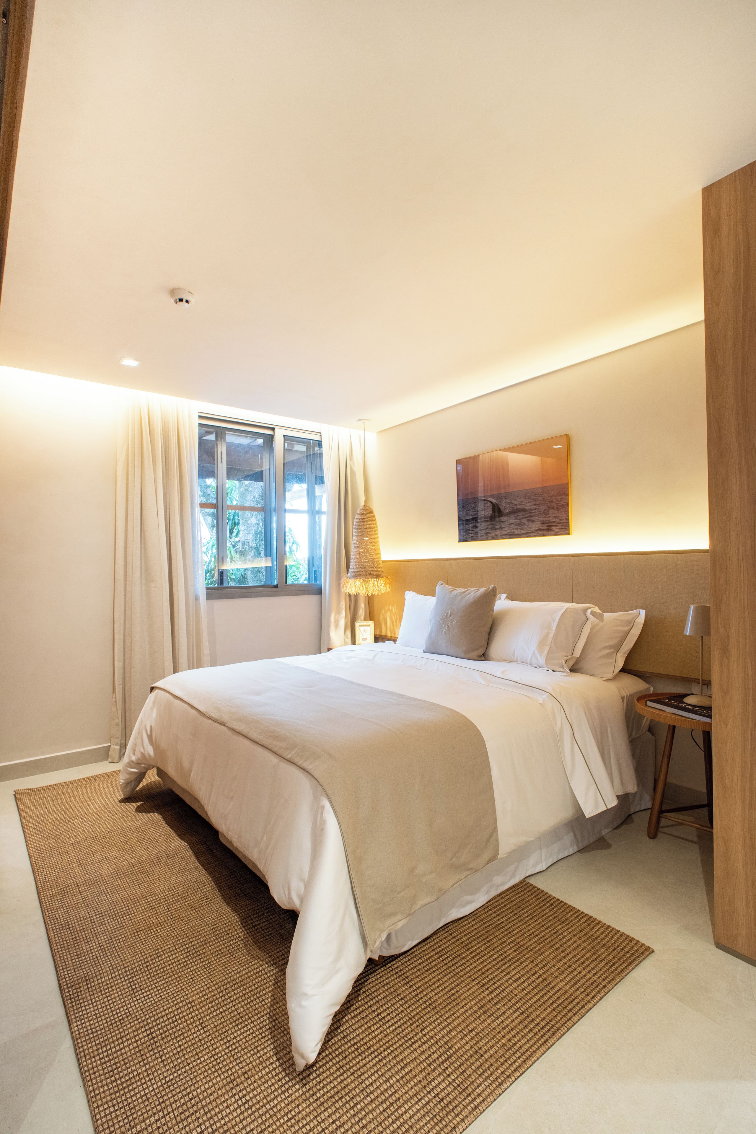 Un dormitorio moderno con una cama grande, una mesita de noche, una lámpara y vistas al exterior a través de una ventana.
