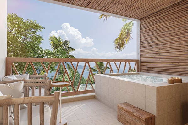 Un balcón con baranda de madera, un jacuzzi y vistas al mar y a los árboles.