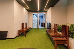 A hallway with a green carpet, wooden benches, and a glass door leading to a bathroom. - Imares by Bhomy (São Paulo)