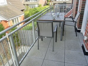 Ein Balkon mit Tisch und Stühlen, einem Metallgeländer und Blick auf benachbarte Häuser.