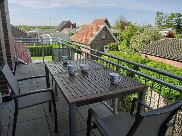 Ein Balkon mit Tisch und Stühlen, einem Geländer und Blick auf angrenzende Häuser.