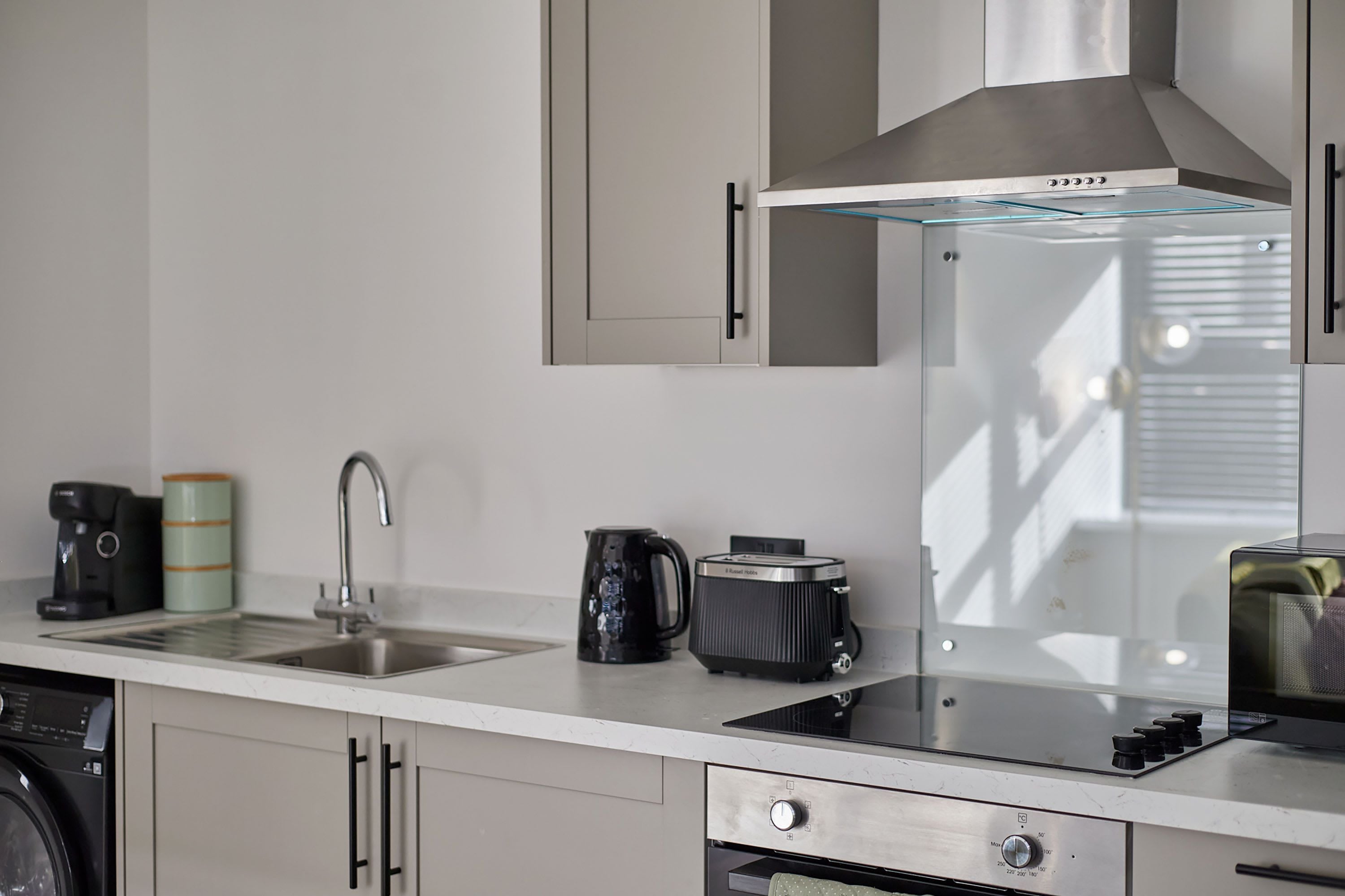 A modern kitchen with a built-in oven, a coffee maker, a kettle, and a toaster.