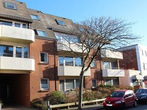 Ein mehrstöckiges Wohngebäude mit Balkonen, ein Baum im Vordergrund und Autos vor dem Haus.