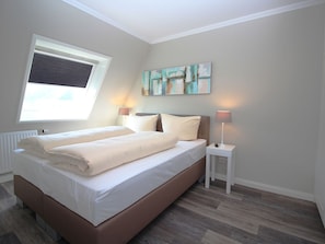 Ein Schlafzimmer mit einem Bett, Nachttischlampen, einem Fenster und einem Gemälde an der Wand.