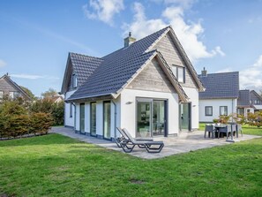 A modern two-story house with a sloped roof, large glass doors, and a patio area with outdoor furniture. - Holiday Home in De Koog With Swimming Pool (De Koog)