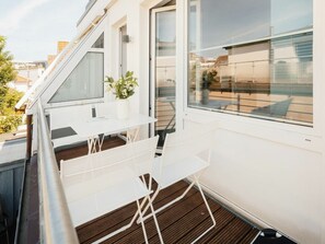 A balcony with a white table and chairs, a potted plant, and a view of the cityscape. - Holiday Apartment With 2 Bedrooms (Norderney)