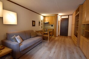 A compact living space with a sofa, a dining table, and a kitchenette. - Des Alpes 15 Studio Apartment MhD (Madonna di Campiglio)