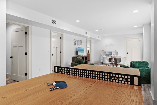 A modern living room with a wooden dining table, a TV, and a green sofa. - 🐾The Lookout at Betty | Heated Pool & Covered Balconies & Pet Friendly & Bikes🚲 (Santa Rosa Beach)