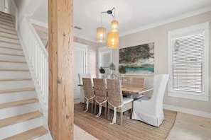A dining area with wicker chairs, a white table, and a painting on the wall. - 🌴St. Somewhere | 5BR Beach Home | Resort Pool + Balconies | 30A ☀️ (Inlet Beach)