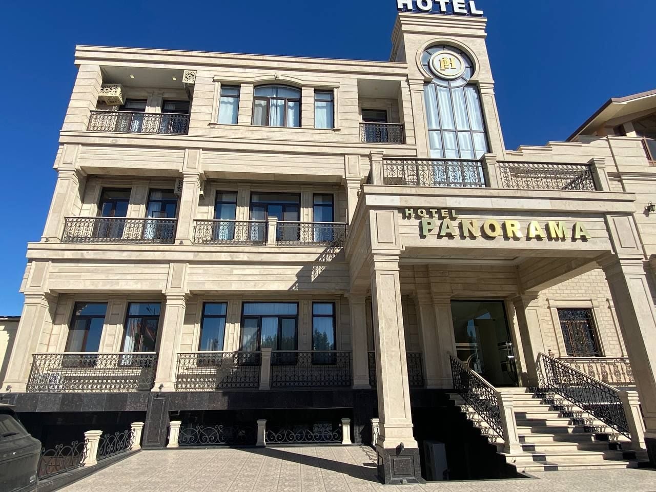 Un hotel de estilo arquitectónico clásico, con una imponente torre de reloj, una entrada principal con escalinata y varios balcones con barandillas de hierro forjado.