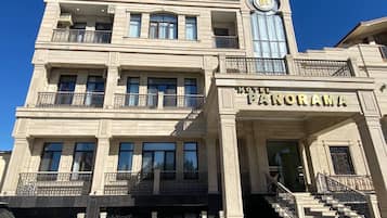 Un hotel de estilo arquitectónico clásico, con una imponente torre de reloj, una entrada principal con escalinata y varios balcones con barandillas de hierro forjado.