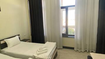 Una habitación de hotel con dos camas, una ventana con cortinas y una pequeña mesa.