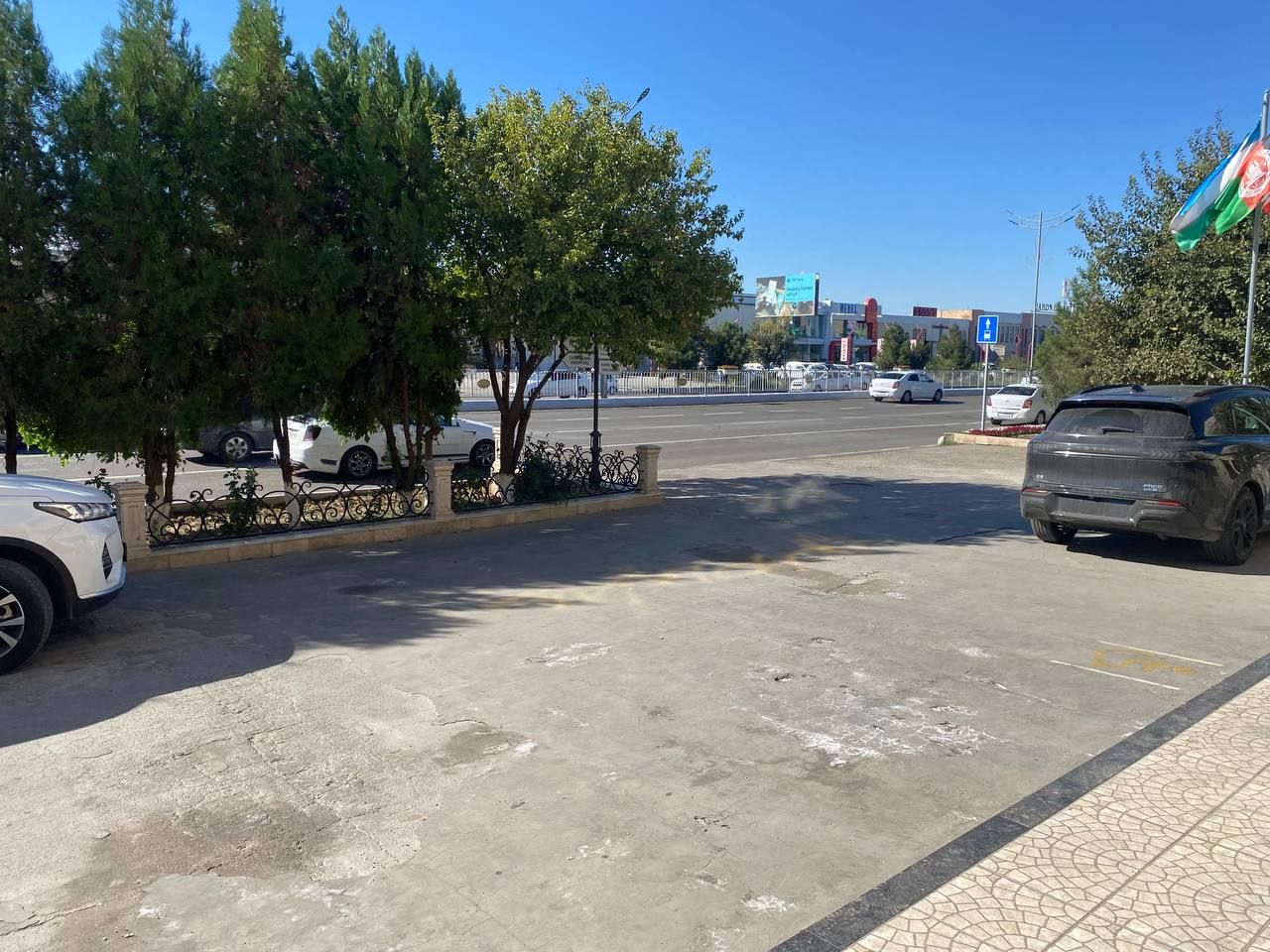 Un estacionamiento con coches, árboles y un edificio al fondo.
