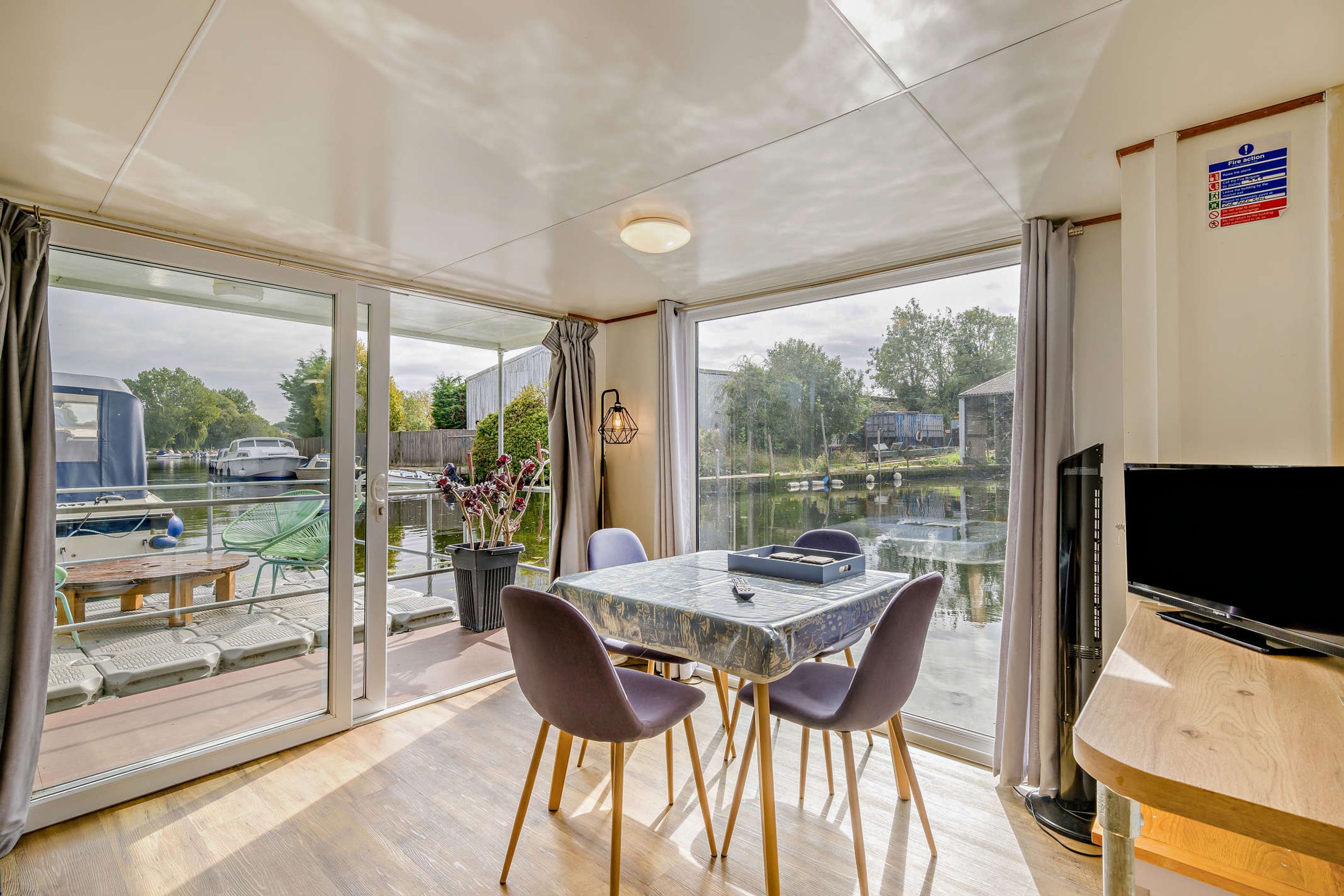 Un comedor moderno con una mesa, sillas, televisor y vista a un puerto deportivo a través de amplios ventanales.